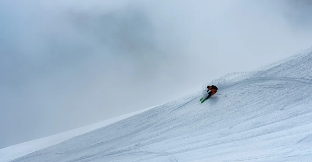 Skitourenfahrer bei der Abfahrt mit Wolken im Hintergrund. Foto von Clement Delhaye-Unsplash