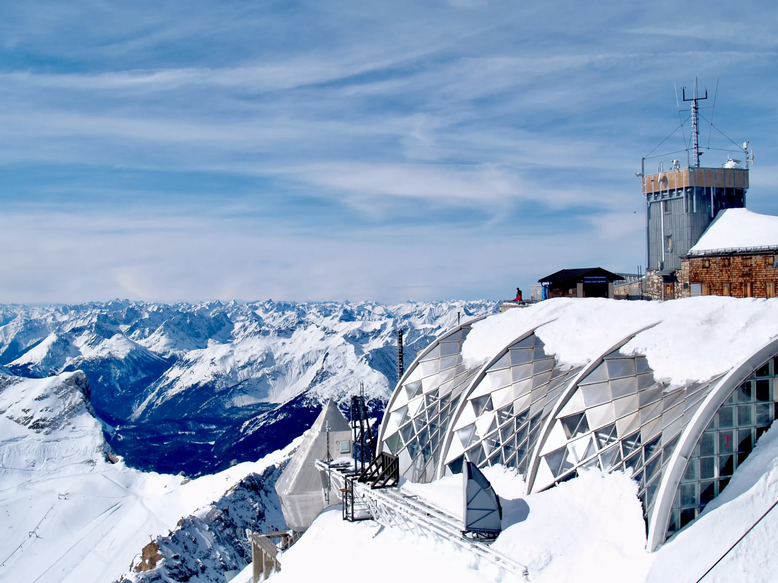 Schutzhütte mit Schnee bedeckt, teilweise mit blauem Himmel und Wolken sowie Berge im Hintergrund. Foto von Peter Burdon-Unsplash