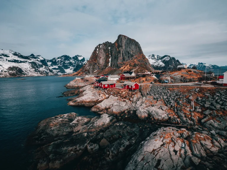 Lofoten mit den typischen roten Häusern am Wasser, Berge und Wolken im Hintergrund. Foto von John O'Nolan-Unsplash