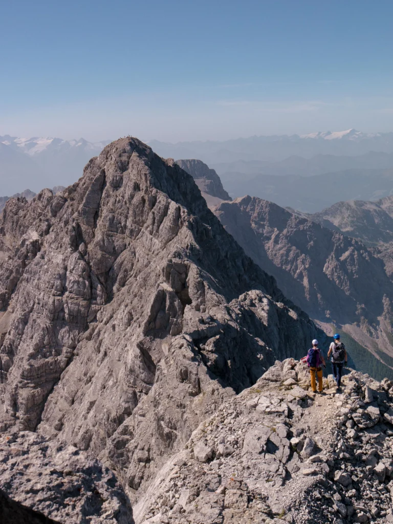 Zwei Bergsteiger am Grat des Watzmann mit blauem Himmel im Hintergrund. Foto von Colin Moldenhauer-Unsplash